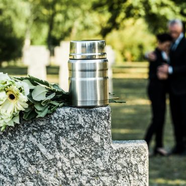 selective focus of white flowers and cemetery urn on tombstone
